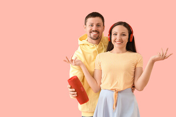 Young couple with headphones and portable speaker on pink background