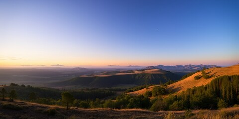 Rolling hills bathed in warm sunset light with distant mountains and a clear blue sky