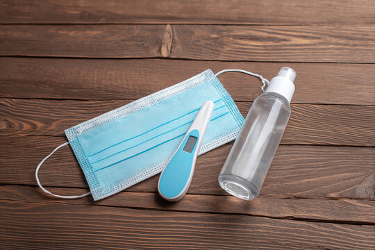 Medical face mask, thermometer and sanitizer on wooden background