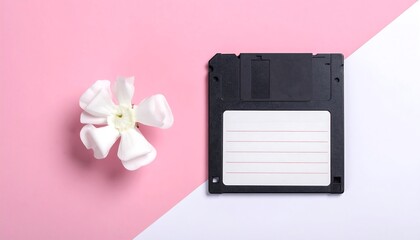 An overhead shot presents a flower alongside a retro floppy disk set against a diagonal split background of pink and white