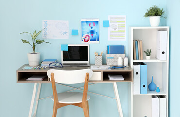 Medical student's workplace with blank laptop and study materials near blue wall in clinic