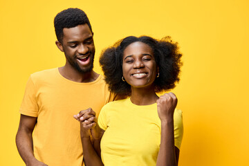Fototapeta premium Happy young couple celebrating success in matching outfits against a vibrant yellow background, expressing joy and love