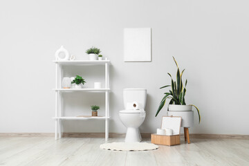 Interior of light restroom with toilet bowl, shelf unit and plants