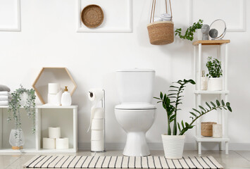 Interior of light restroom with toilet bowl, shelf units and plants