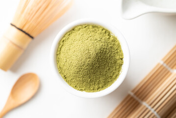 Top view of matcha green tea powder with wooden spoon, bamboo whisk and Chawan bowl on white background