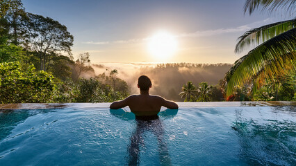 A person relaxing in an outdoor infinity pool surrounded by tropical jungle, soft morning mist rising, turquoise water reflecting golden sunrise, tranquil mood, wide panoramic shot from behind, sense 