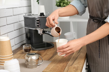 Young female barista pouring coffee from jug into disposable cup in coffee shop
