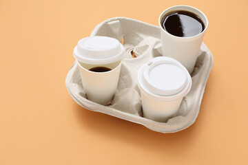 Disposable cups of coffee in holder on orange background