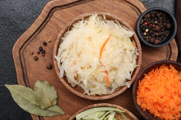Delicious sauerkraut in bowl with ingredients on black background. Top view
