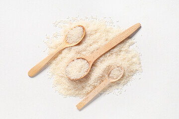 Wooden spoons with raw rice on white background