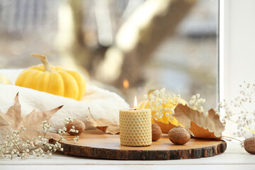 Burning candles with autumn leaves, nuts and flowers near window in room, closeup