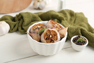 Bowl with baked garlic, rosemary and peppercorns on white wooden background