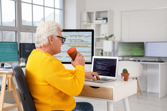 Senior programmer with coffee and laptop working at table in office - Powered by Adobe