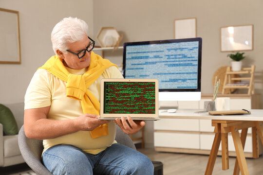 Senior programmer with laptop sitting at table in office
