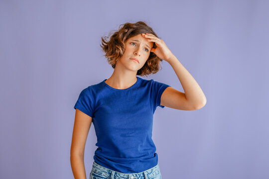 Thoughtful teenage girl holding head with stressed expression and anxious vibe for emotional concepts on vibrant blue studio background with mental health focus