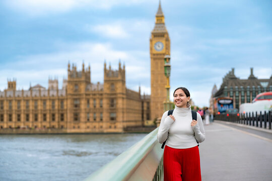 Happy young Latina woman walks along Westminster Bridge in London, England, with Big Ben in background. Dressed a red skirt, white turtleneck, she enjoying cultural exploration in the British capital