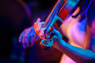 Close-up of woman hands playing violin under colorful stage lights