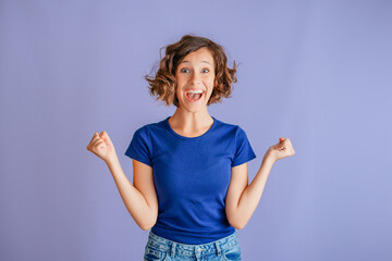 Excited teenage girl laughing with open mouth in joyful surprise reacting to good news on vibrant blue studio background in excited moment