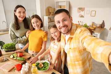 Happy parents with their daughters taking selfie while cooking in kitchen