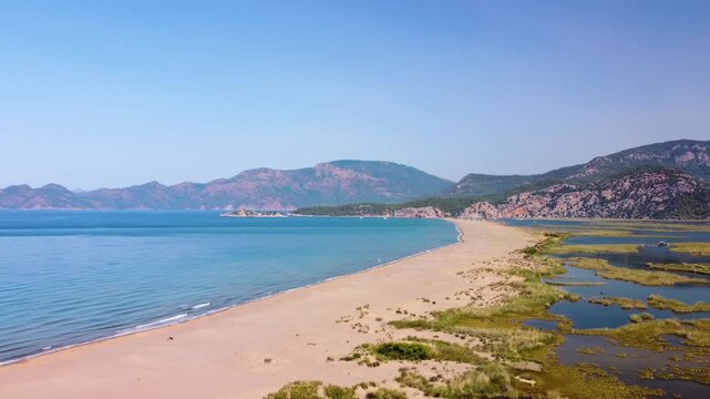 natural beauty of Iztuzu Beach in Dalyan, Turkey, from an aerial perspective. This stunning footage captures the pristine golden sands, the tranquil turquoise waters of the Mediterranean Sea on one si