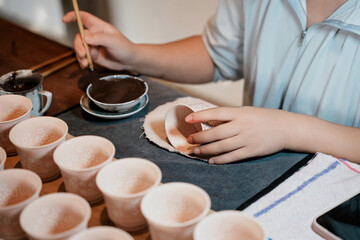 Person Handcrafting Ceramic Cups with Brush and Ink