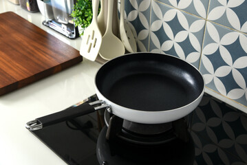 A non-stick frying pan with a white exterior and black handle sits on a black gas stovetop in a modern kitchen