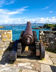 A cannon points out toward a body of water under a bright blue sky