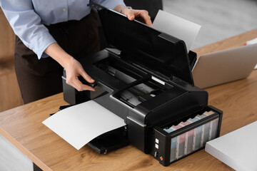 Young businesswoman using printer on table in office, closeup
