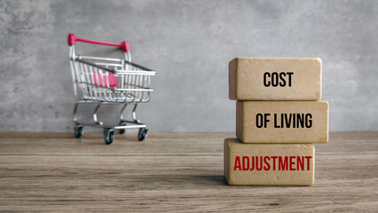Cost of Living Adjustment (COLA) Concept: Stacked Wood Blocks and a Miniature Shopping Cart on a...