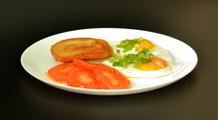 Two fried eggs with green onions, tomatoes and bread croutons on a black background.