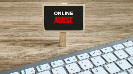 ONLINE ABUSE Warning Message in Red and White Text on Chalkboard Above Computer Keyboard on Wooden...
