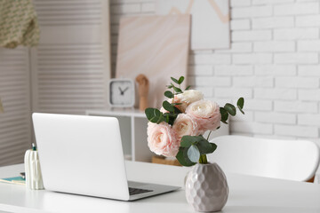Stylish workspace with modern laptop and beautiful flowers in light home office