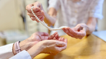 高齢女性がパールネックレスを渡す女性の手