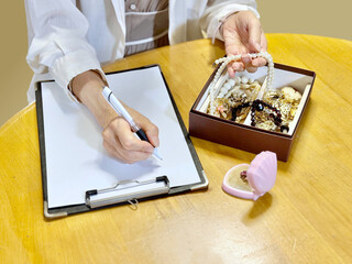 箱に入ったアクセサリーを持って用紙に記入する女性の手