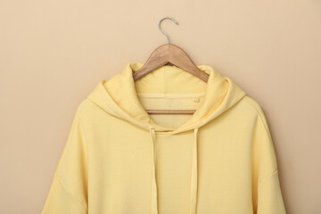 Hanger with stylish yellow hoodie on beige background