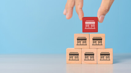 Hand choose wooden block stack in pyramid with franchise business store icon for franchising to growth branch expansion and business banking loan.