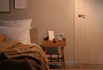 Alarm clock with blank frame on table in bedroom at night