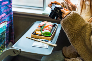 Young Asian woman using digital camera taking picture of traditional Japanese food lunch box bento while travel on train in winter season. People commuter travel on public transportation.