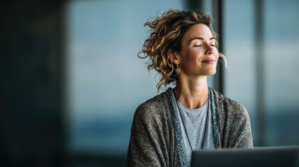 A woman with curly hair wearing a gray sweater, sitting in front of a laptop with her eyes closed, appearing to be meditating or deep in thought.