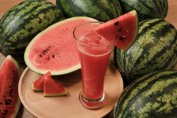 Close-up shot of half pieces of fresh red watermelons and glass of smoothie on wooden dish, natural...