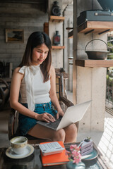 A woman sits in a cafe, focused on her laptop, surrounded by rustic decor and natural light.