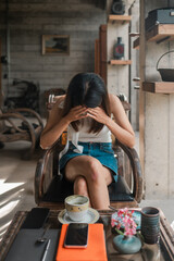 A woman in a modern cafe, holding her head in her hands, with coffee and smartphone on the table, conveying stress or contemplation.