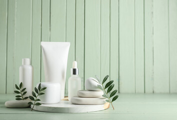 Composition with spa stones, green leaves, jar and bottles of cosmetic products on green wooden background, closeup