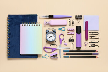 Different school stationery supplies and alarm clock on beige background
