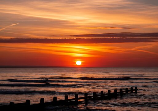 Seaside serenity a mesmerizing sunset illuminates the tranquil ocean and wooden breakwater structure creating