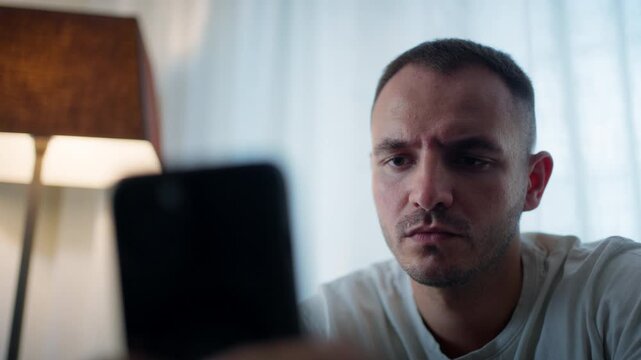 Young man bored in living room looking at phone, feeling apathetic