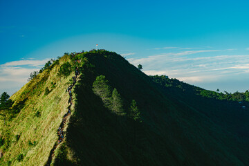 A scenic view of a grassy mountain ridge under a clear blue sky, with a visible hiking trail along the peak.