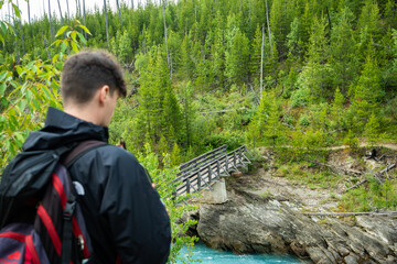 A hiker pauses on a trail, gazing at a weathered bridge