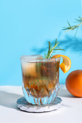 Glass of tasty Old Fashioned cocktail with rosemary on white table against blue background