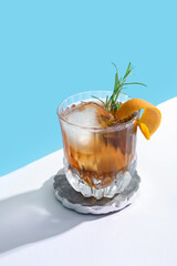 Glass of tasty Old Fashioned cocktail with rosemary on white table against blue background